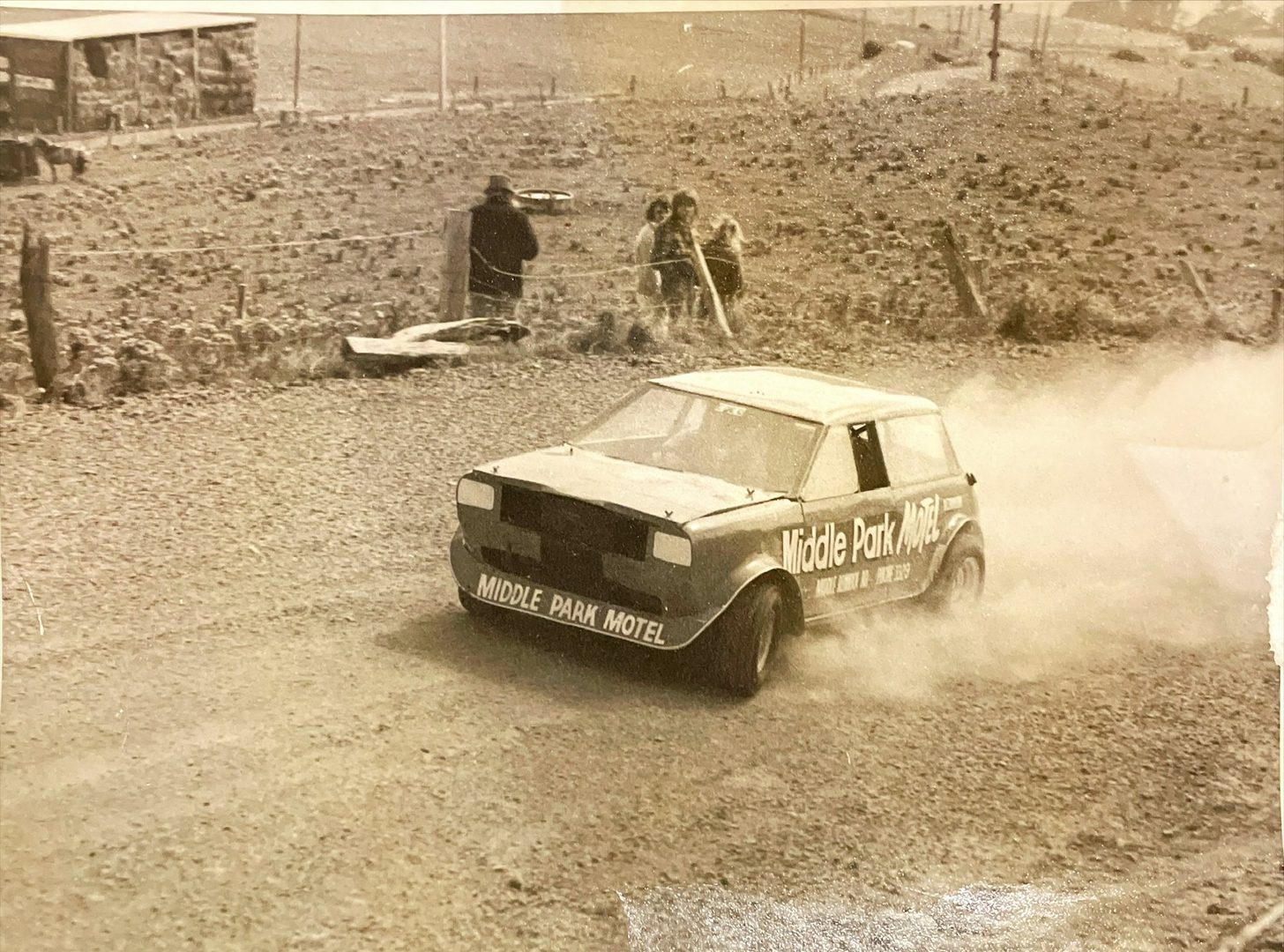 The Middle Park Motel Mini Sprint throwing up gravel past spectators at a farm fence