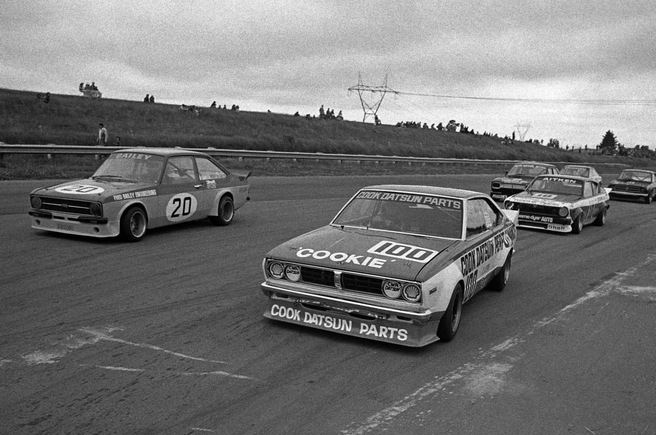 Reg Cook's Datsun #100 on the front of a saloon grid beside Bailey's #20 Escort, Aitken's #10 behind