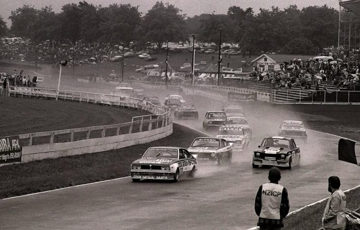 Reg Cook's Datsun #100 leads a saloon field through spray